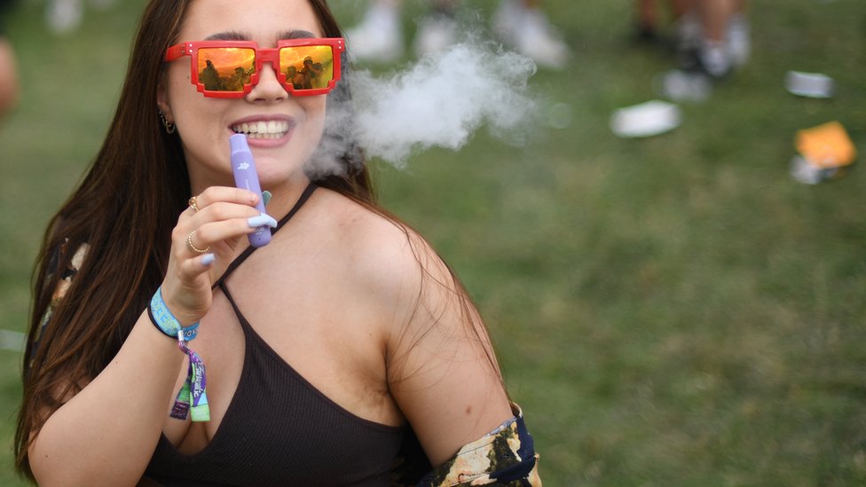 person vaping at music festival, traveling with disposable vape, convenience vaping outdoor - Glastonbury: Disposable vapes added to