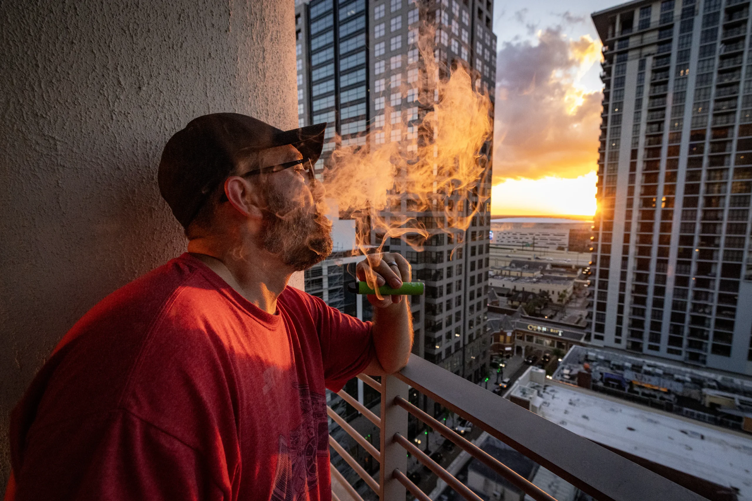 person vaping on balcony Sydney sunset, relaxing vape lifestyle Australia, disposable vape outdoor scene - Man vaping on balcony with city skyline sunset photo – Free Sunset ...
