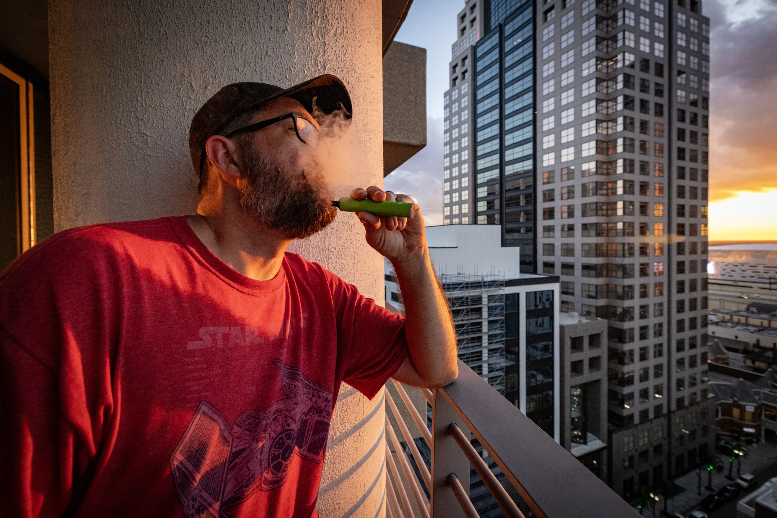 vaping on balcony Sydney sunset, person relaxing vape Australia, Sydney skyline vape lifestyle - Man on balcony vaping with city skyline sunset. photo – Free ...