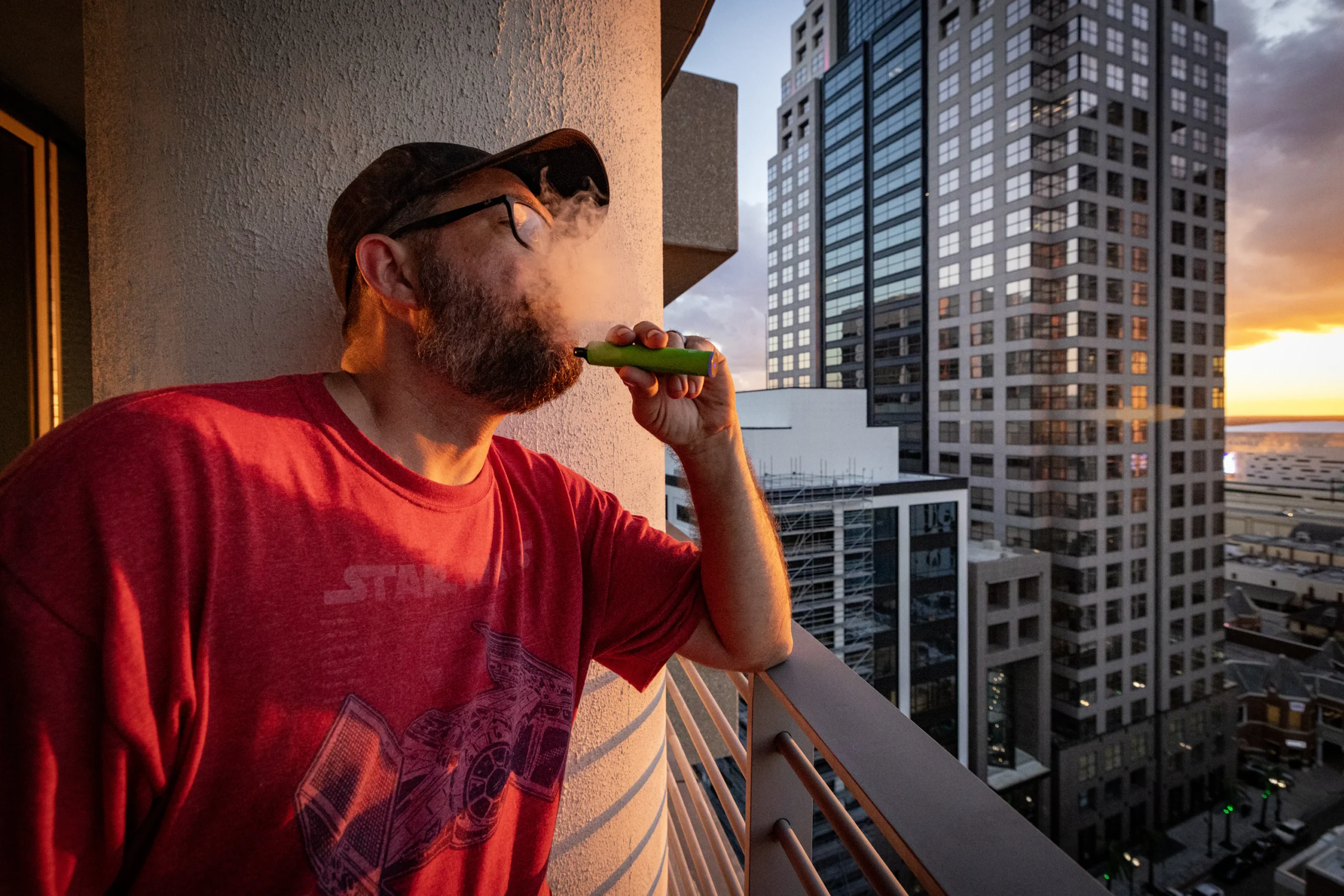 person relaxing balcony Sydney vape - Man on balcony vaping with city skyline sunset. photo – Free ...