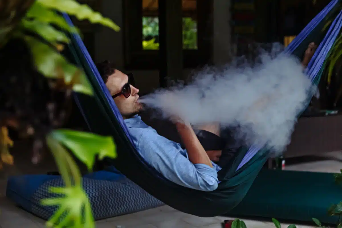 person vaping on sunny Sydney balcony, relaxed coastal view vape Australia, luxury vape experience - Vaping on Vacation - Red Vape